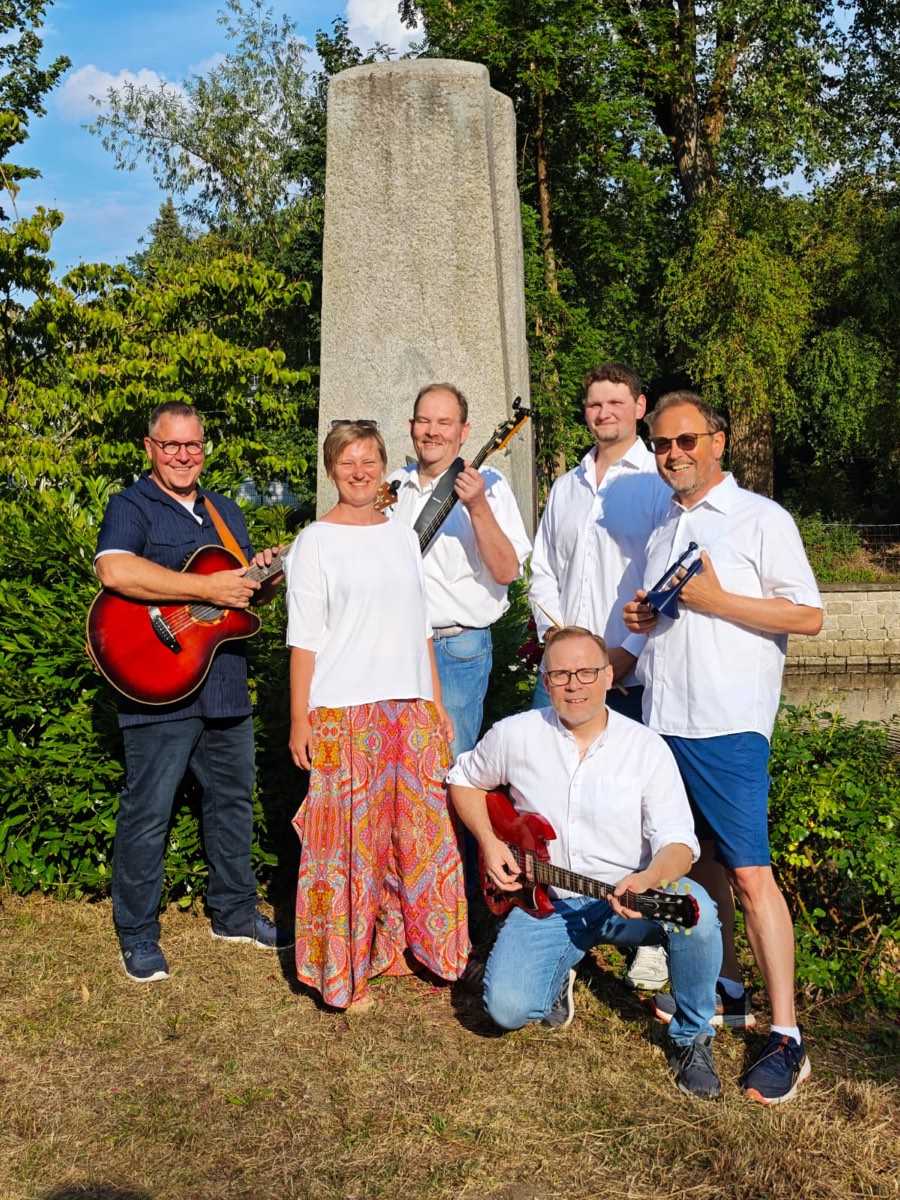Gruppenfoto der Band mit Instrumenten am Wasser